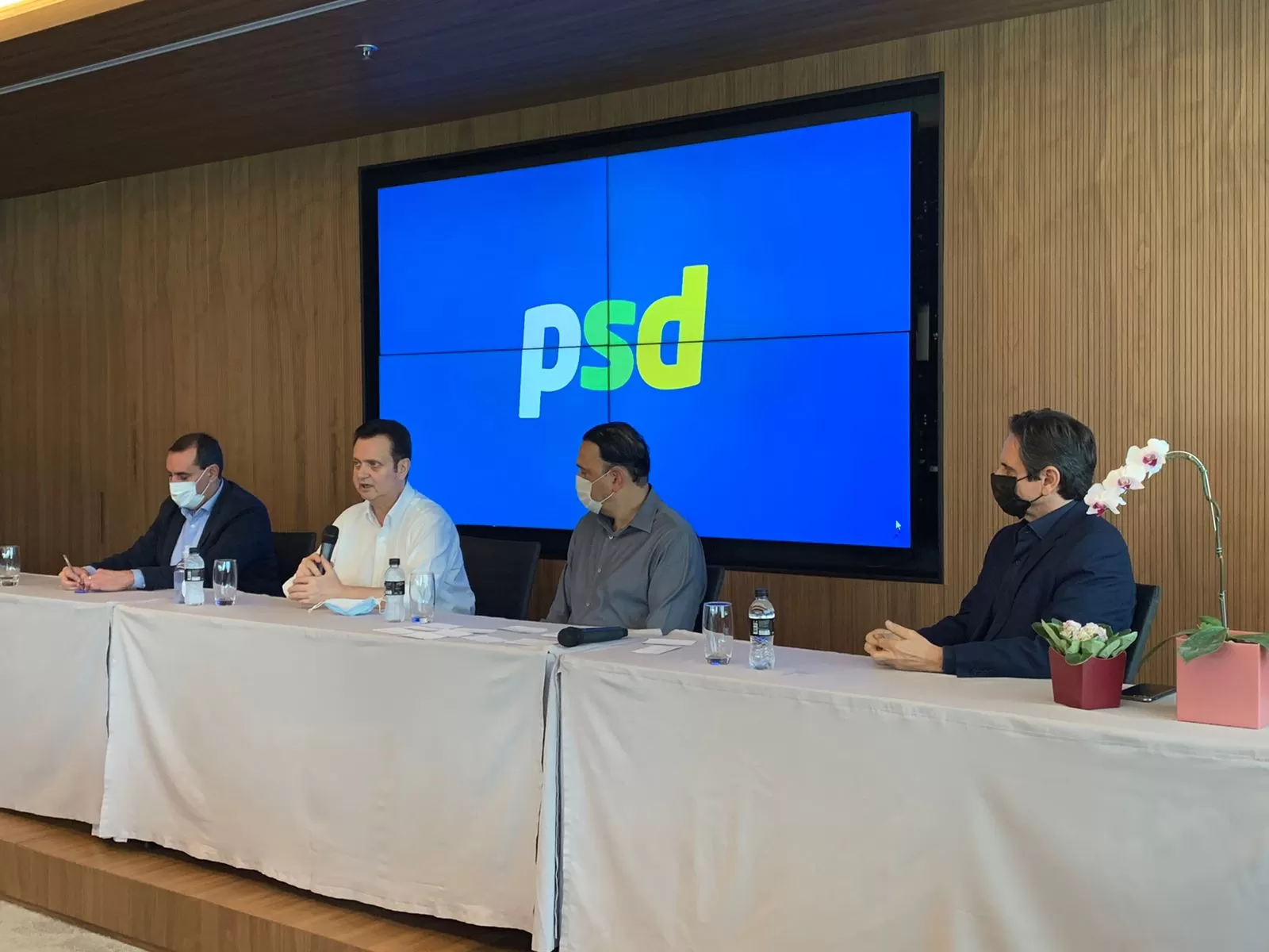 Foto mostra filiados do PSD de São José dos Campos em frente a um telão com o logo do partido (Felicio Ramuth, Anderson Farias e Gilberto Kassab), ilustrando matéria sobre mudança de endereço para o diretório do PSDB.