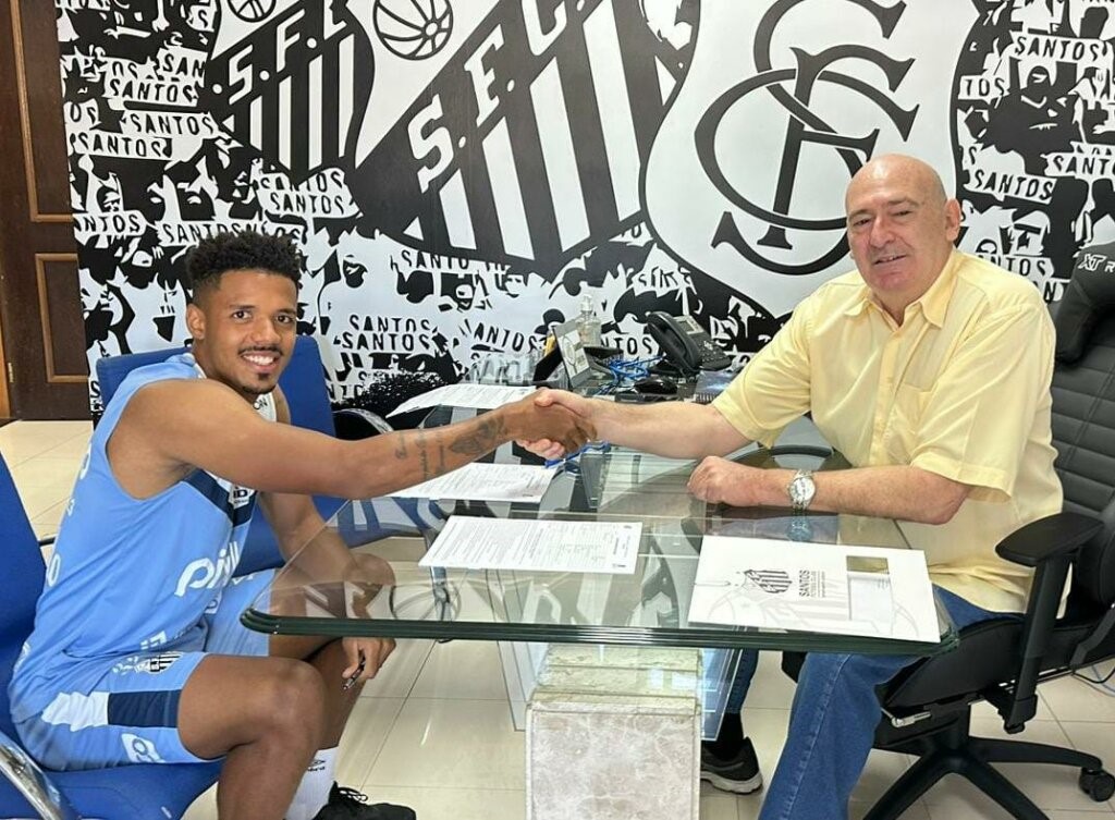 Gabriel Inocêncio com a camisa do Santos sentado em uma cadeira azul com uma mesa de vidro à frente.