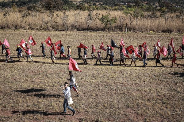 integrantes do MST em campo gramado caminhando com bandeiras