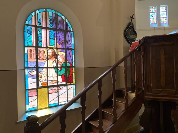 São João e Jesus Cristo durante a Última Ceia, em uma imagem dentro da capela, em vidro, com uma escada de madeira ao lado.