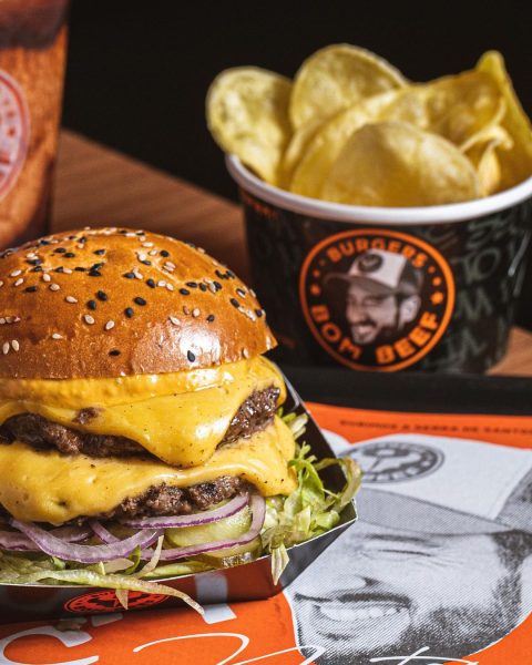 Uma das opções no Bom Beef Burgers, em São José dos Campos, com um lanche no lado esquerdo, com cheddar, pão e alface; ao lado direita há um pote de batata frita; foto ilustra matéria sobre hamburguer artesanal em SJC.