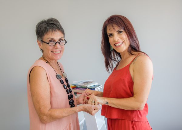 May Parreia (à esquerda) e Tati Iaconelli (à direita), em frente a um fundo cinza; foto ilustra matéria sobre reestreia da coluna Ofício das Palavras.