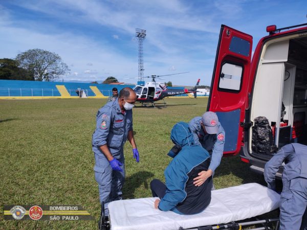 Homem sentado em maca enquanto é atendido por bombeiros