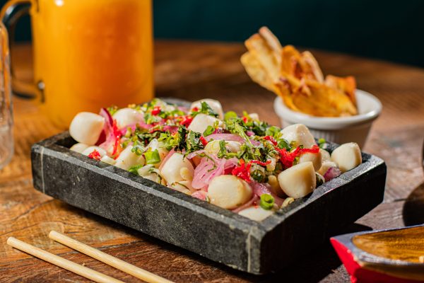 Prato do Marujo Beach Bar, apoiado em uma mesa de madeira, com ingredientes coloridos em cima de uma plataforma preta, com uma garrafa de suco ao fundo; foto ilustra matéria sobre o Festival Gastronômico de São José dos Campos.