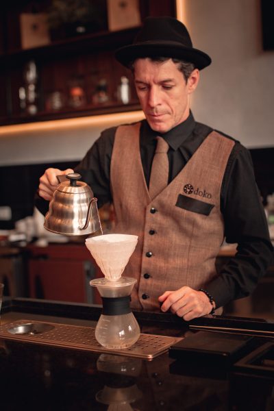 Sandro Marson, da Doko Coffee & Wine, de São José dos Campos, com uma camisa preta, gravata marrom e chapéu; foto ilustra matéria sobre o Dia Nacional do Café.