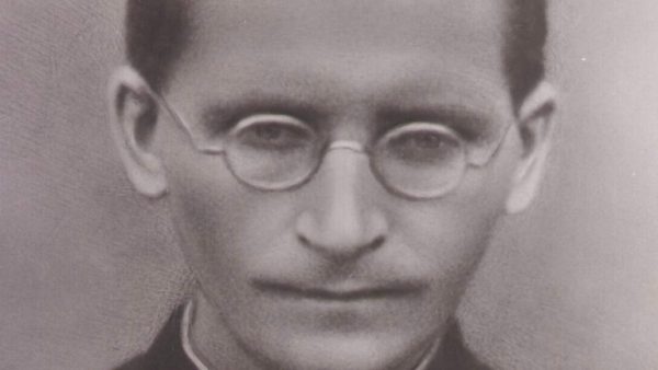 Retrato do Padre Rodolfo Komorek, em preto e branco; na foto ele utiliza um óculos e uma roupa preta, enquanto olha para a câmera.