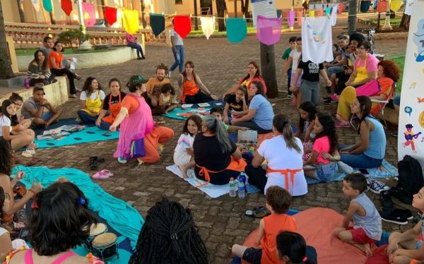 Crianças sentadas no chão ao lado de adultos, durante piquenique literário do projeto Ler é uma Viagem.