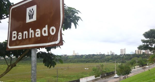 Placa do Banhado, com área verde ao fundo, céu azul e carros passando; foto ilustra matéria sobre a decisão da Justiça sobre regularização do bairro Parque Nova Esperança.