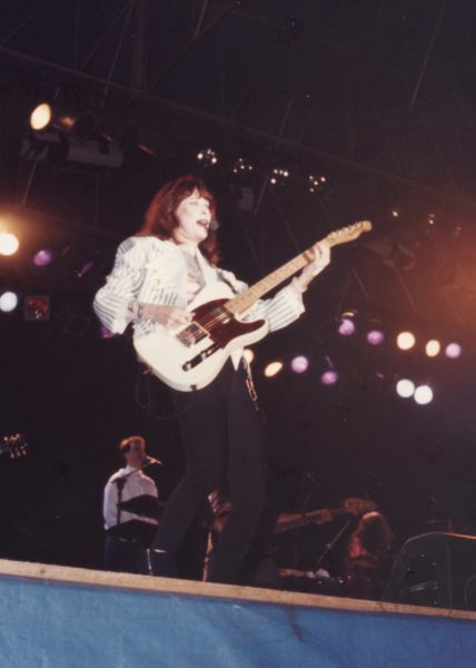 Rita Lee em São José dos Campos, durante apresentação no CenterVale Shopping, em um palco, com uma guitarra na mão e uma jaqueta branca.
