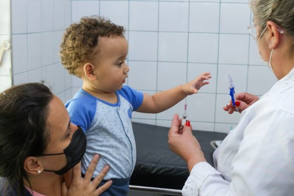 mãe segurando criança pequena para profissional ed saúde vacinar