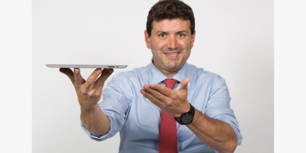 Homem de blusa social azul com gravata vermelha segurando um tablet.