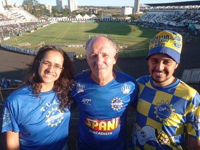 malu, à esquerda, tião marino, no meio, e macedo, na direita, sorrindo para foto com gramado do estádio palma de travassos ao fundo.