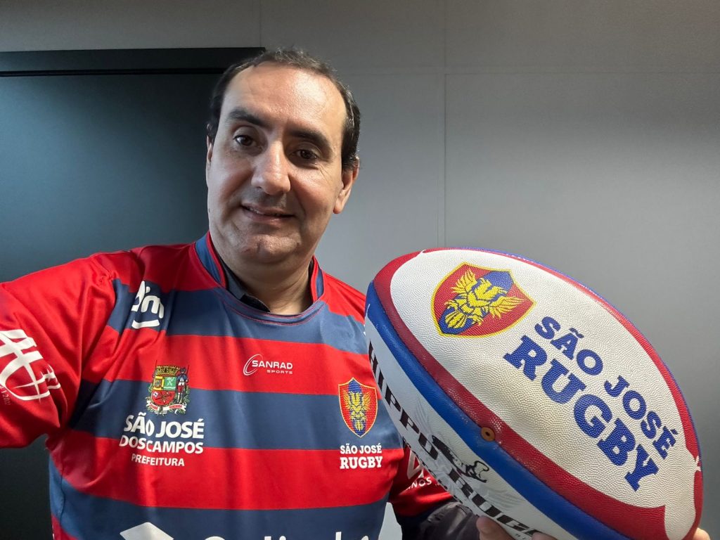 Anderson vestido com o uniforme do São José Rugby e segurando bola personalizada do clube enquanto sorri