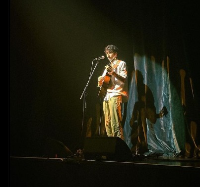 img-responsive Tom Maior Ribeiro, em frente ao microfone tocando violão enquanto canta no Teatro La Cigale, em Paris
