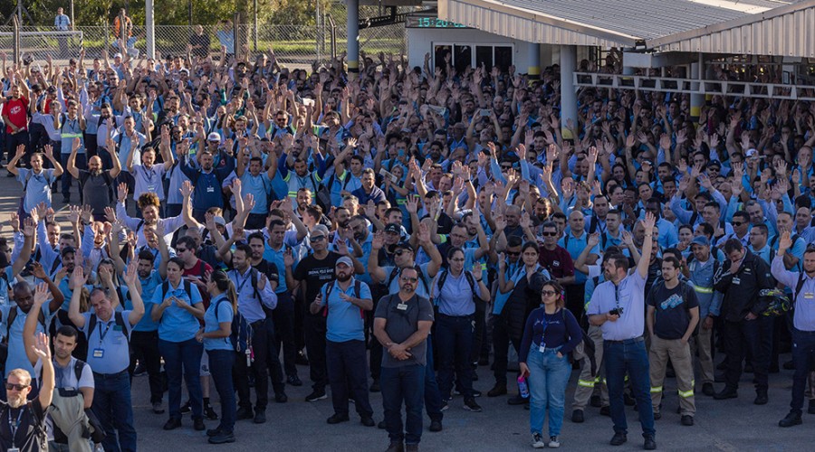 Trabalhadores da GM reunidos com os braços levantados após aceitarem acordo de layoff, feito entre sindicato e a empresa