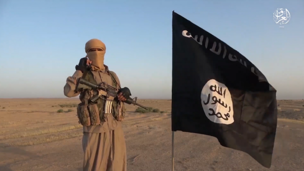 soldado do estado islâmico ao lado de bandeira do grupo terrorista em deserto no iraque em 2021