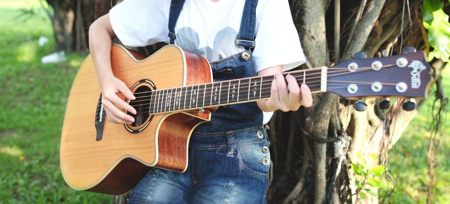 Criança com tocando violão encostada na árvore