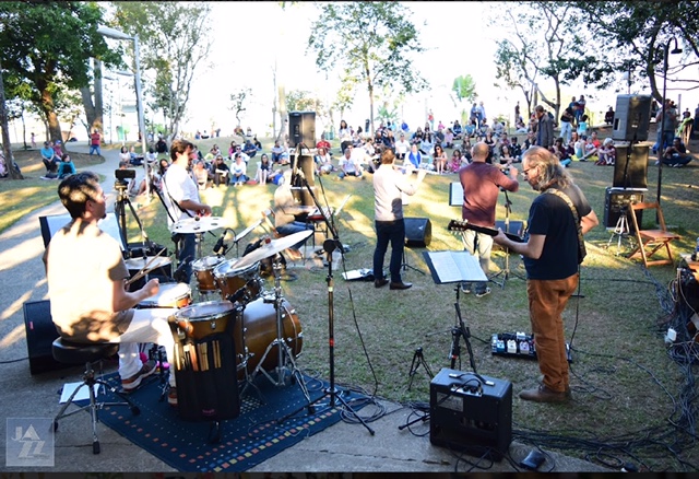 Banda se apresentando em gramado com público no fundo