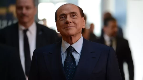 silvio berlusconi de terno caminhando. eleolha para a frente e sorri.