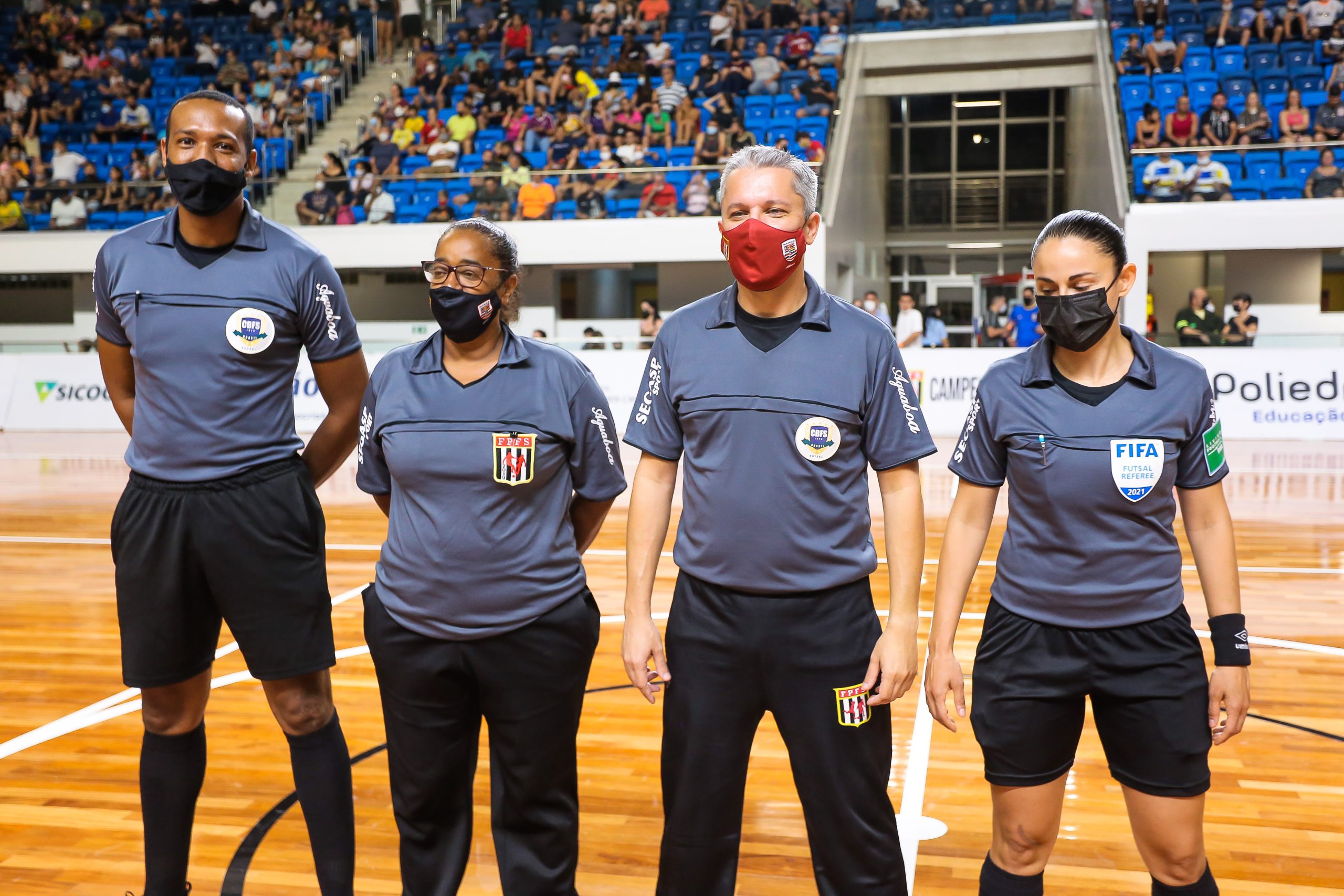 Arbitragem posicionada em quadra antes de iniciar a partida de futsal, utilizando máscaras no rosto. São José oferece vagas para curso de arbitragem.