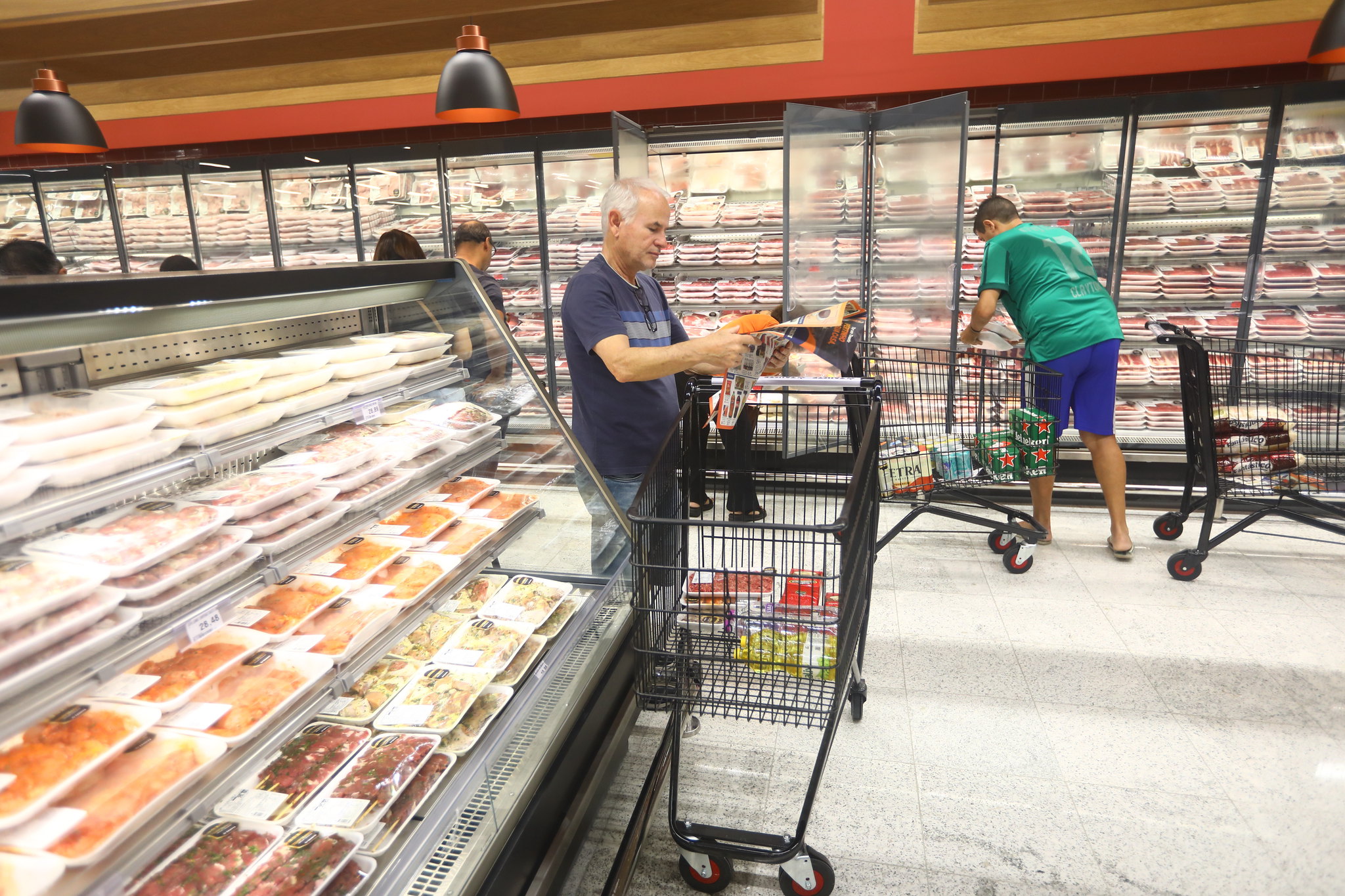 cliente conferindo preço de produto ao lado de seu carrinho de compras em supermercado