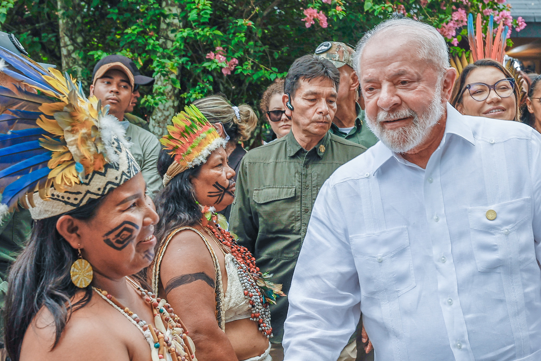 número de viagens de Lula é superior as de Bolsonaro nos primeiros seis meses de mandato; presidente Lula à direita e duas mulheres indígenas da Colômbia à esquerda com diversas pessoas ao fundo