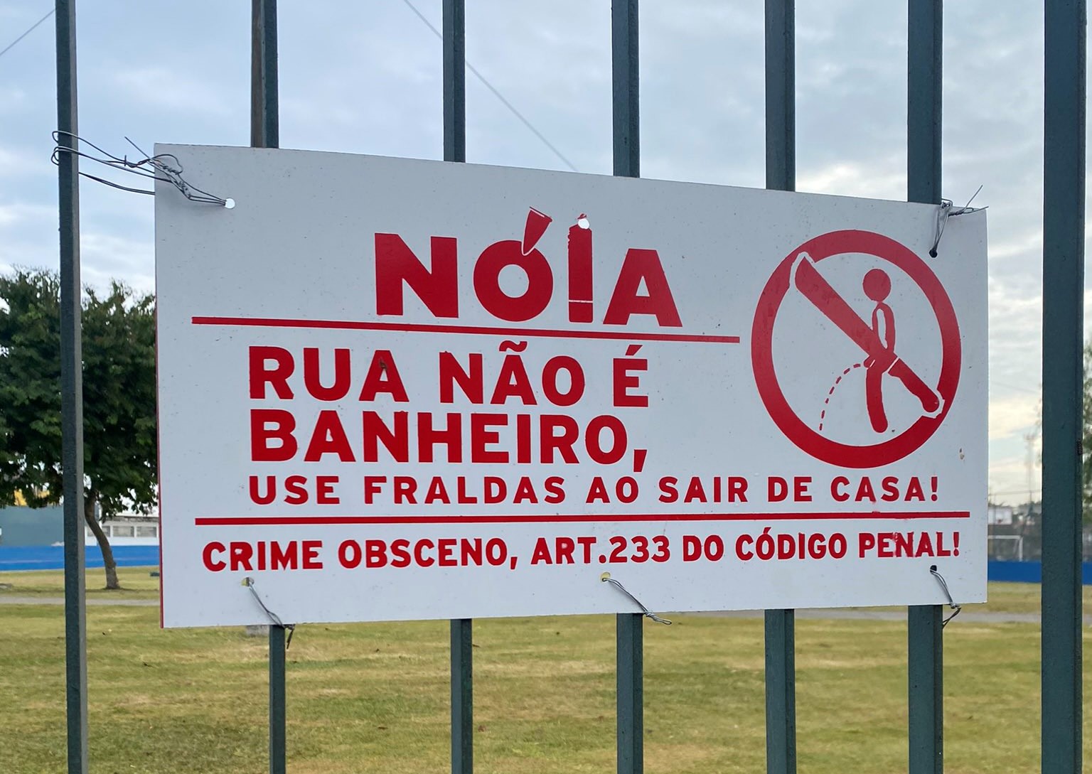 placa encontrada nas grades laterais ao poliesportivo do campo dos alemães, em sjc, que faz aviso: 'nóia, rua não é banheiro, use fraldas ao sair de casa', tem imagem de boneco urinando e facão atravessando o boneco e cita ainda o código 233 do código penal