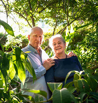 Fotógrafo Sebastião Salgado e a esposa lado-a-lado no meio de uma mata com sol iluminando