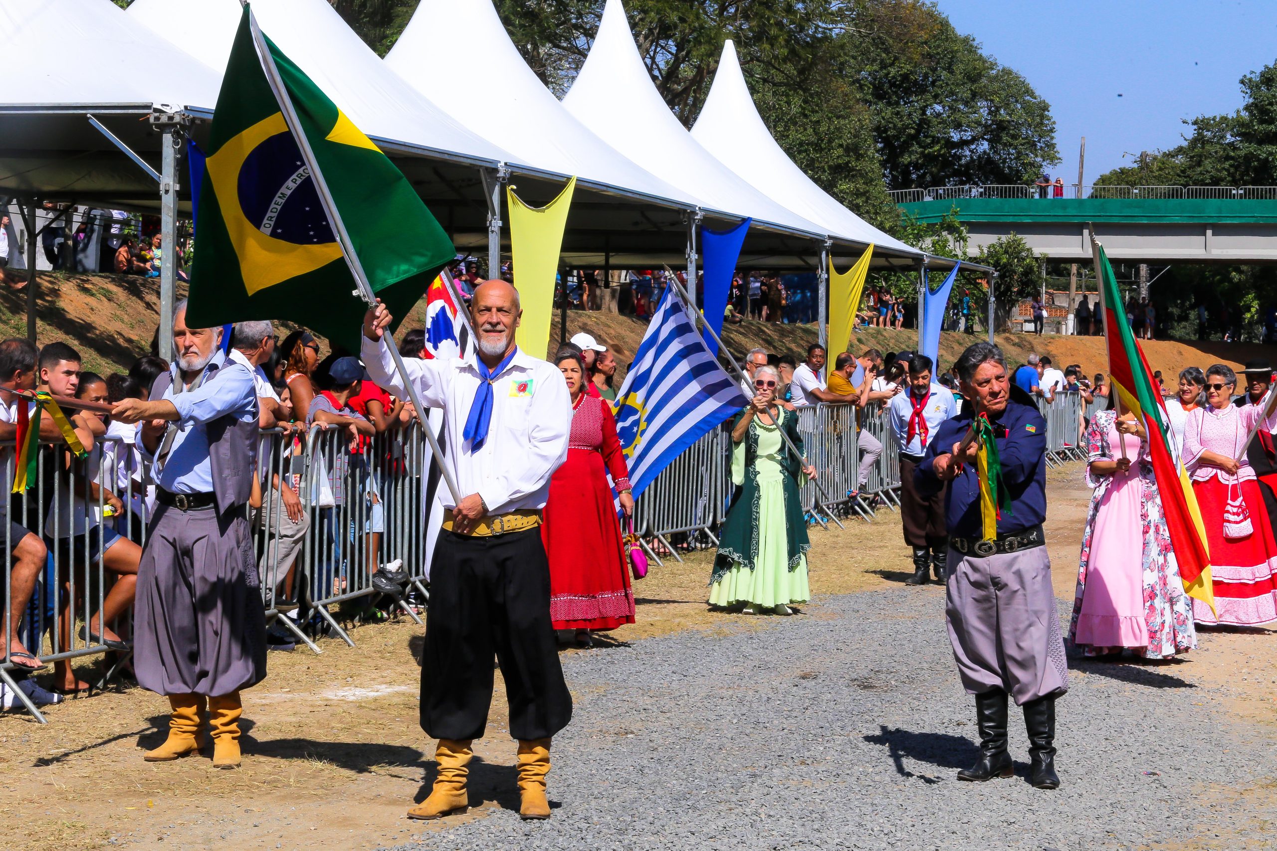 Pessoas em pé com bandeiras durante desfile de aniversário de Eugênio de Melo