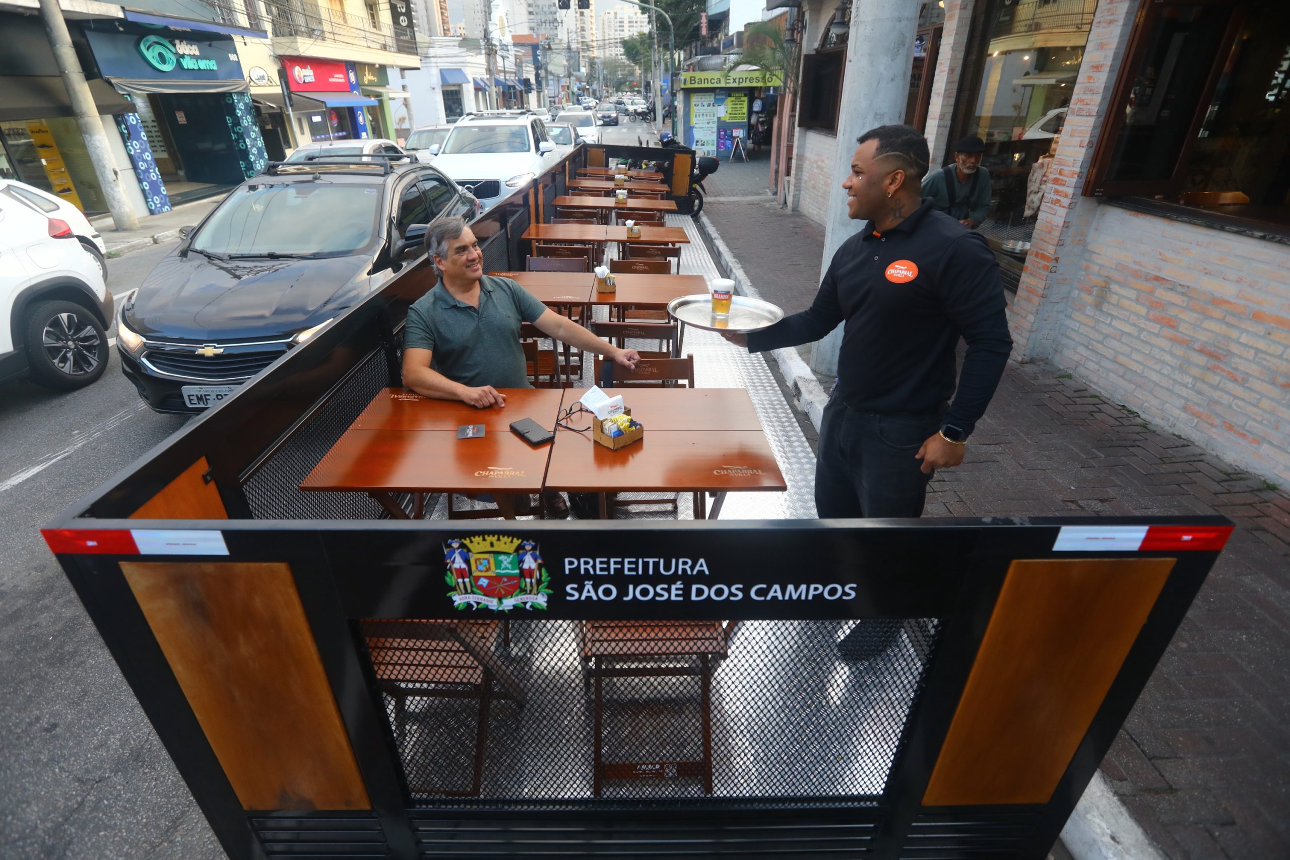 Homem sentado sendo servido por garçom. Programa de parklets sendo usado pela primeira vez em São José dos Campos.