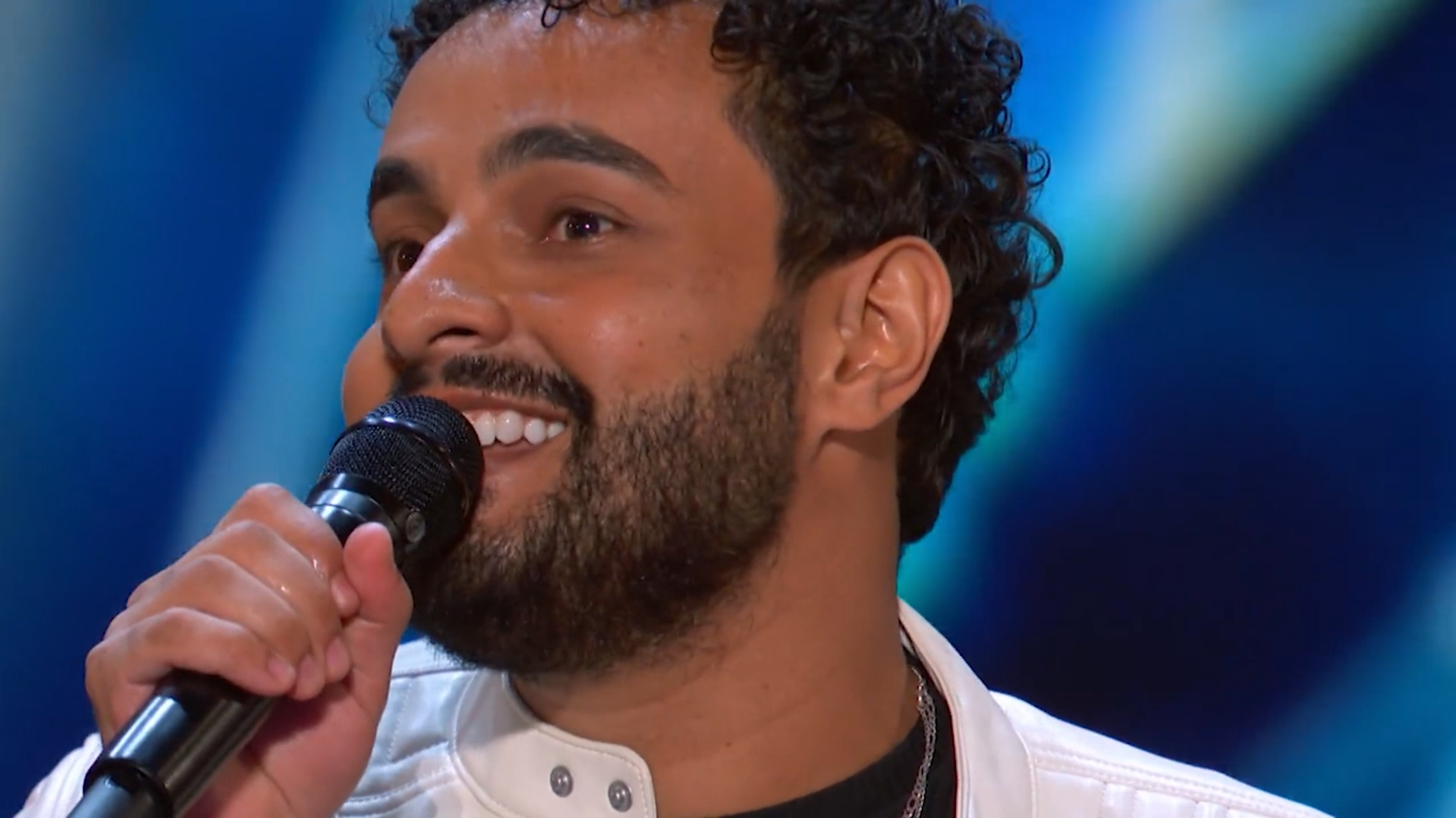 Brasileiro cantando com microfone em programa de talento norte-americano. O brasileiro surpreendeu os jurados e o público do programa e ganhou o botão dourado