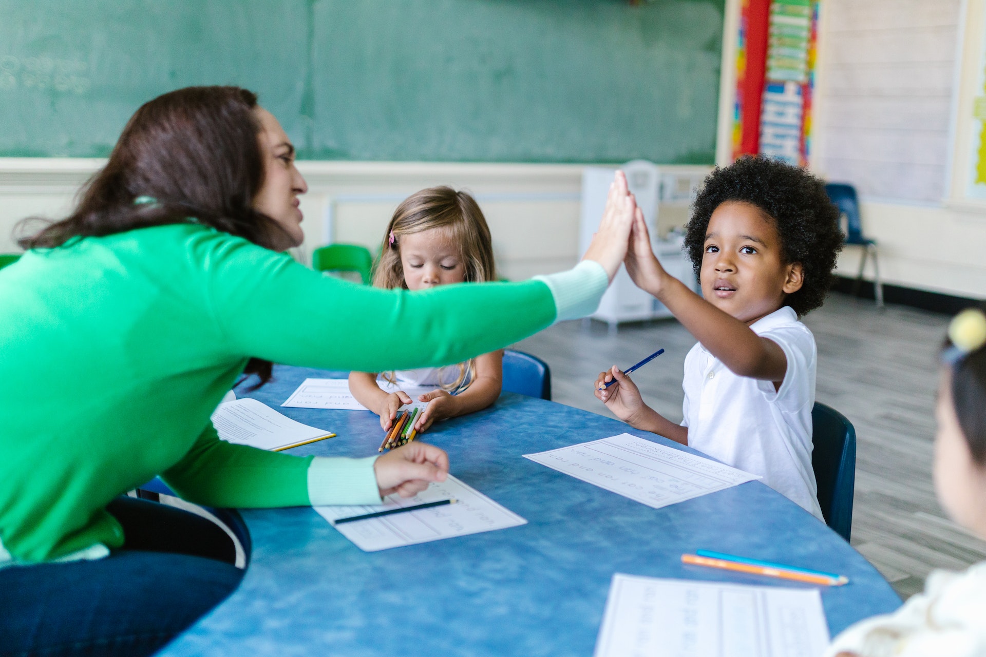 professora batendo na mão de aluno em sala de aula e outros alunos ao redor. crianças tem cerca de 2 anos de idade.