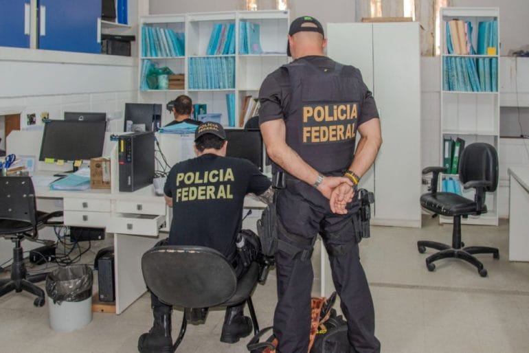 Policiais federais analisando papéis em escritório do paço municipal de Ubatuba; PF apura fraudes na merenda escolar de Ubatuba
