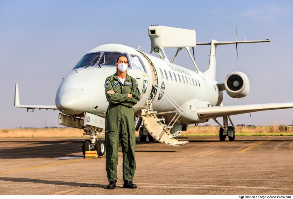 Pessoa de máscara, em pé, em frente a um avião