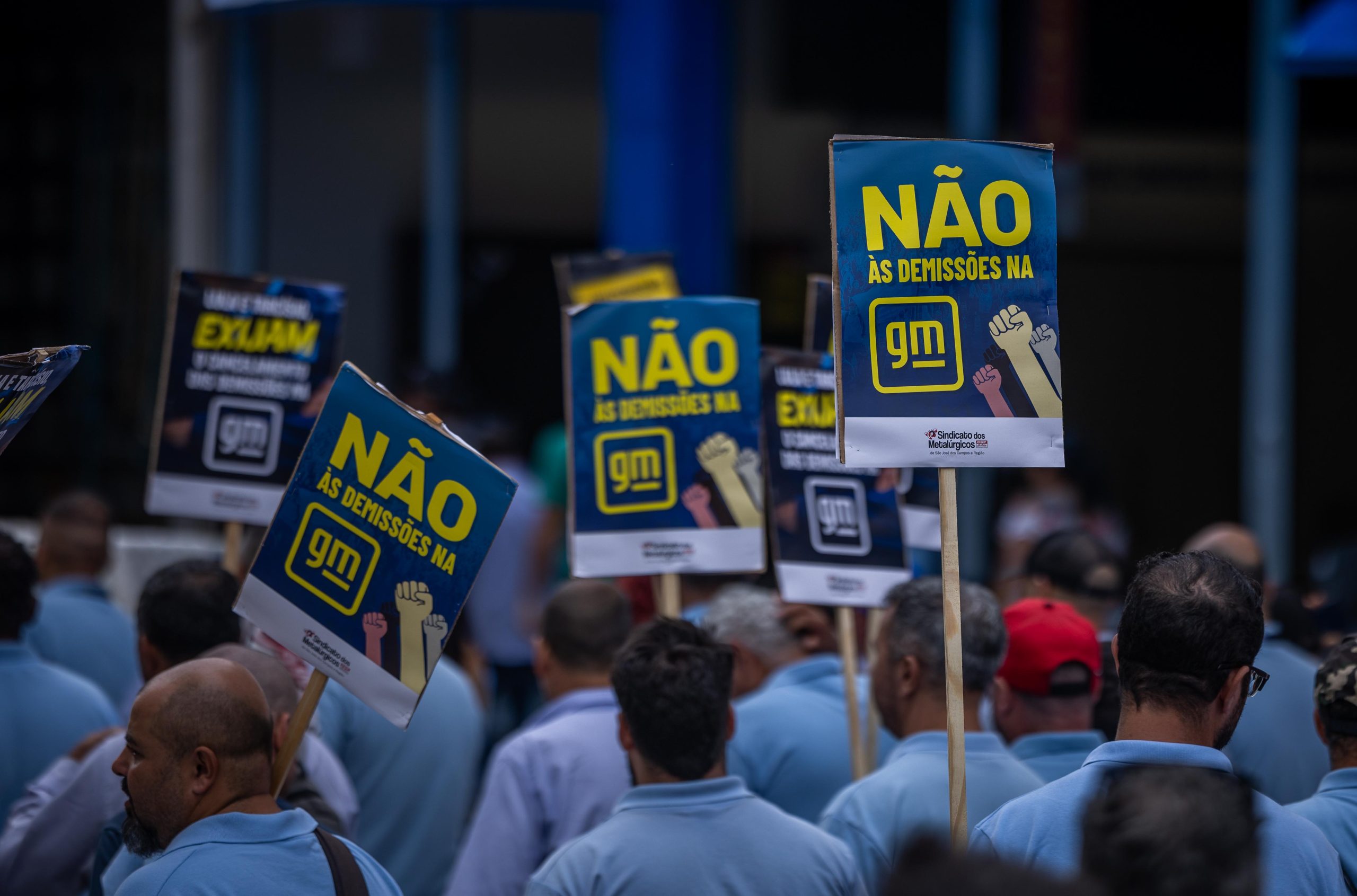 metalúrgicos protestando, com placas pedindo o cancelamento das demissões, durante audiência com a gm