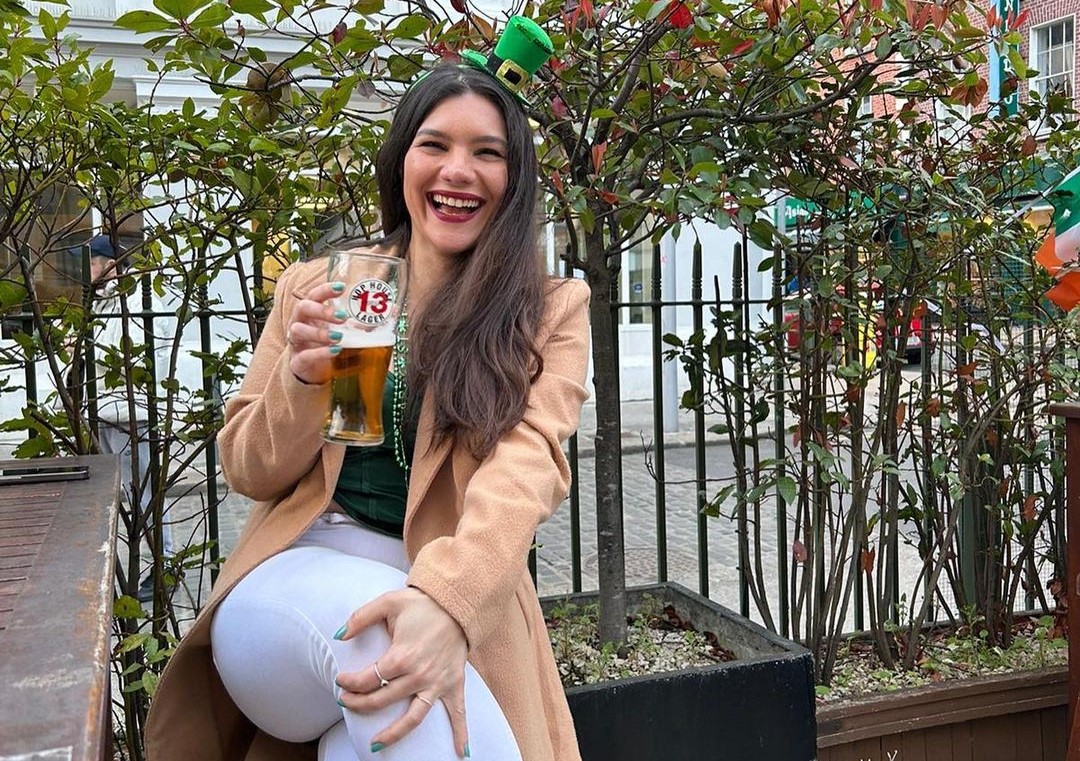 josilaine sorrindo enquanto segura uma caneca de cerveja sentada em banco na irlanda
