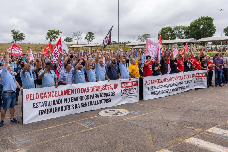 Trabalhadores da GM que decidiram continuar em greve após cancelamento de demissões em São José; eles estão reunidos com as mãos levantadas em protesto