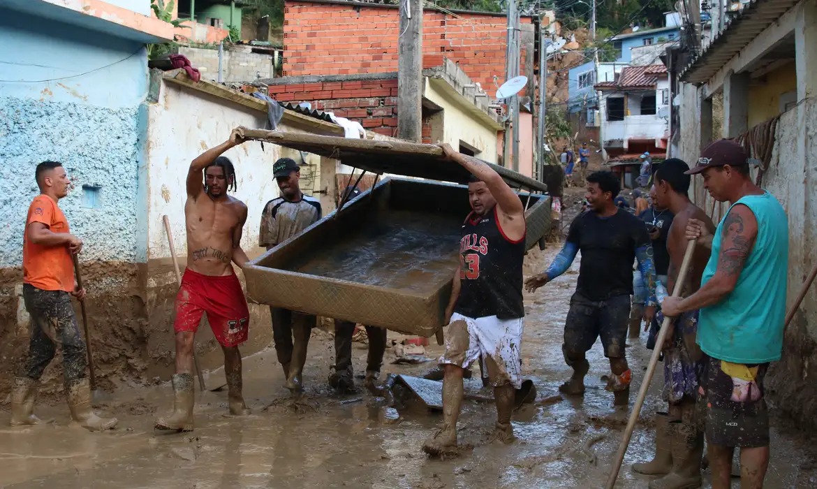 Homens carregando móvel após deslizamento de terra atingir casas em tragédia causada pelas chuvas em São Sebastião; MP e Defensoria Pública