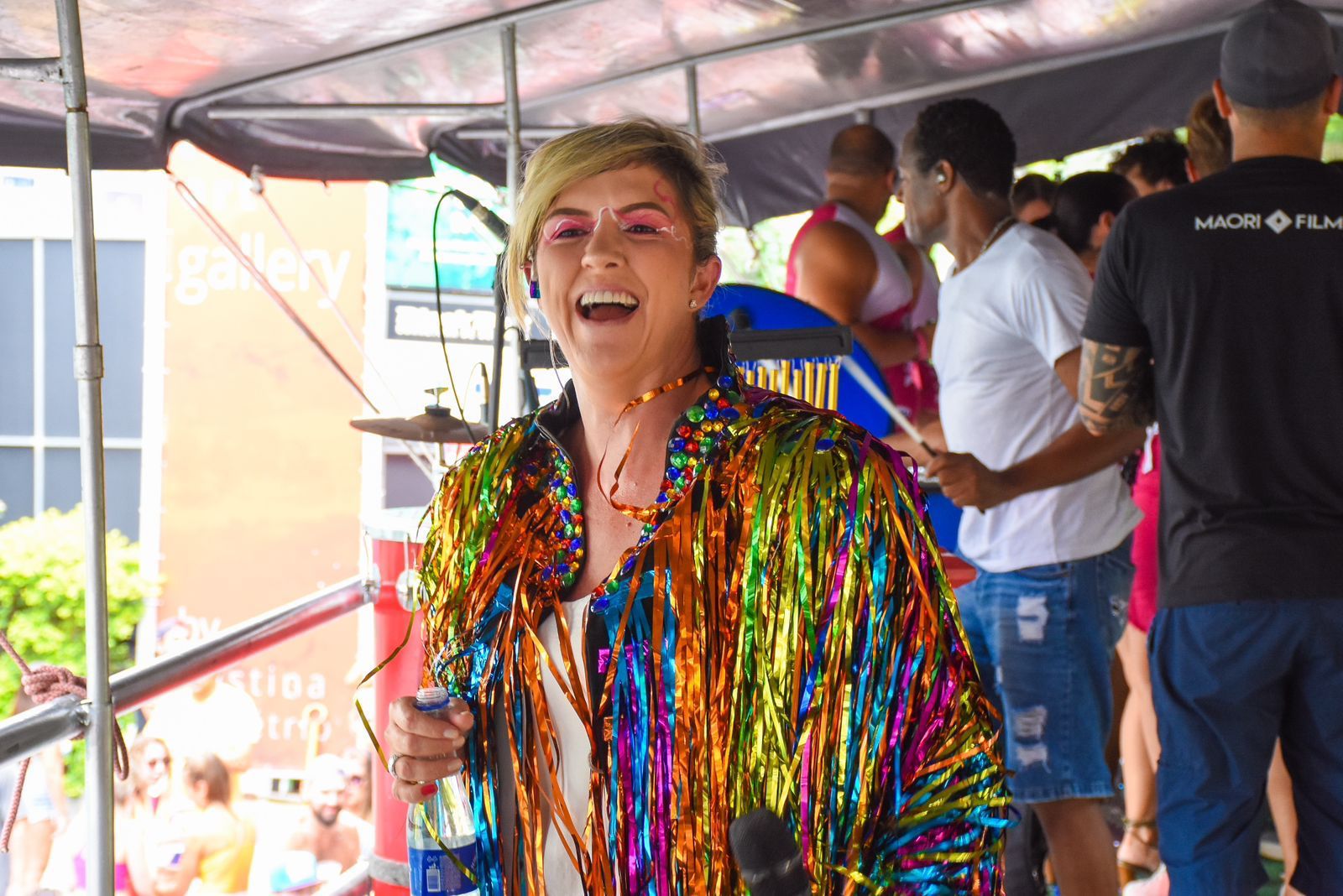 priscilla couto com roupa cheia de fitas coloridas sorrindo em dia de sol em cima de trio elétrico