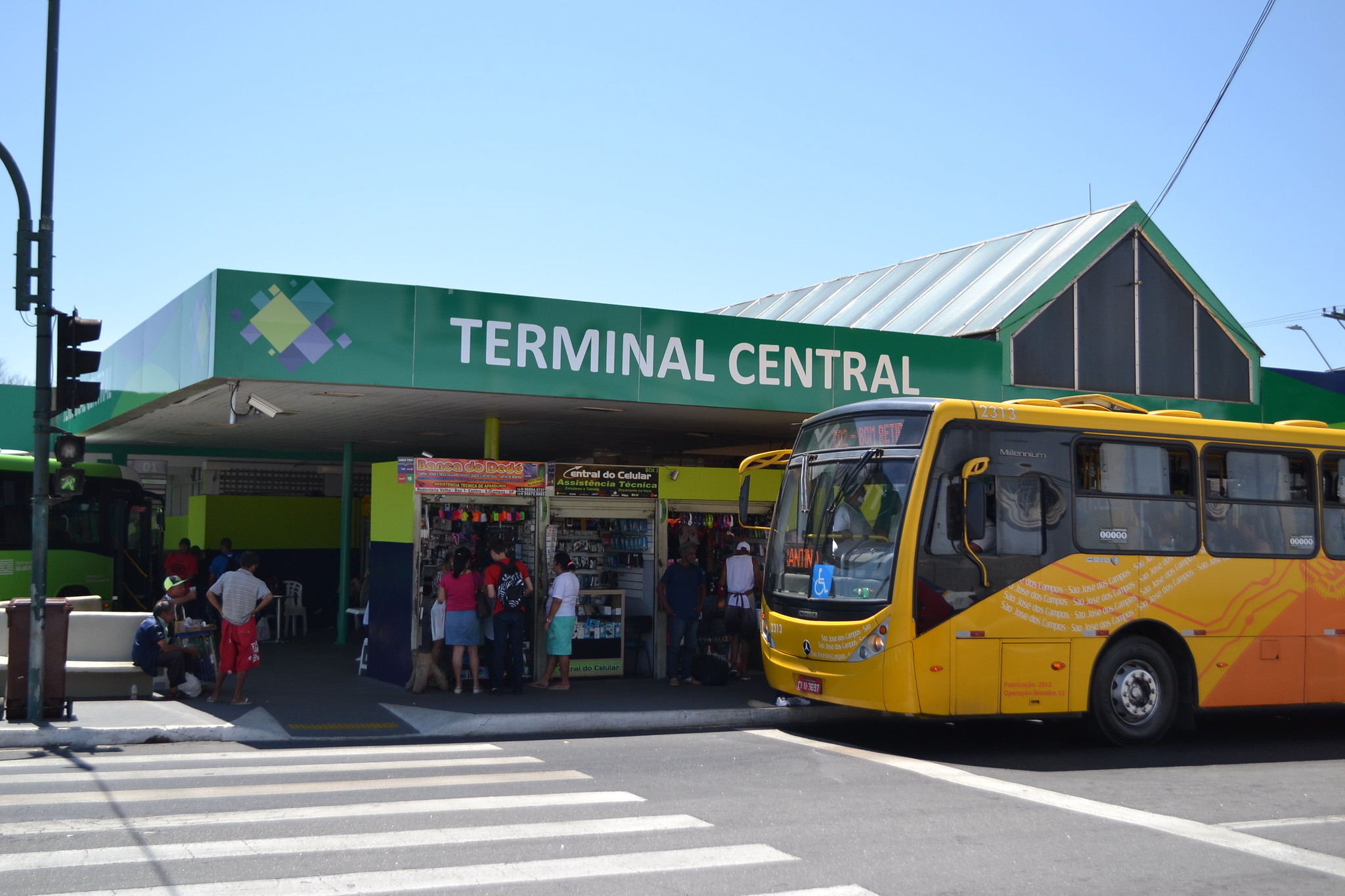 fachada lateral do terminal central de são josé dos campos em dia ensolarado e movimentado com ônibus amarelo parado em frente