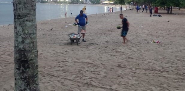 homens recolhendo lixo com carrinho de mão em praia de caraguá