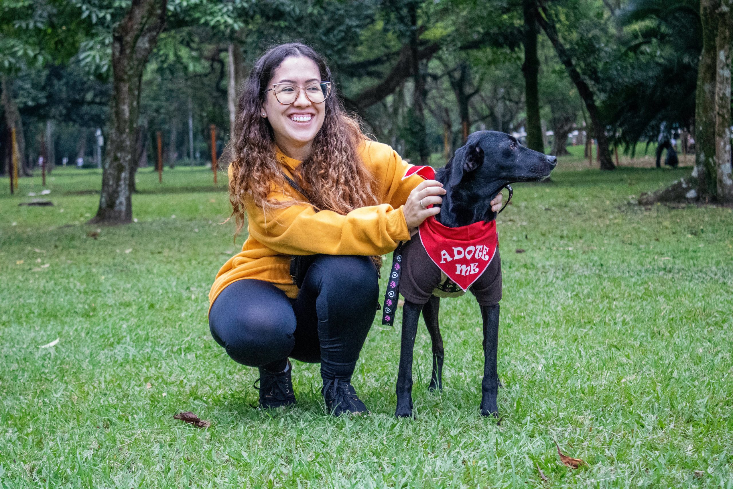 Mulher agachada com cachorro, que veste uma flanela "adote-me", uma referência ao processo da feira de adoção em taubaté