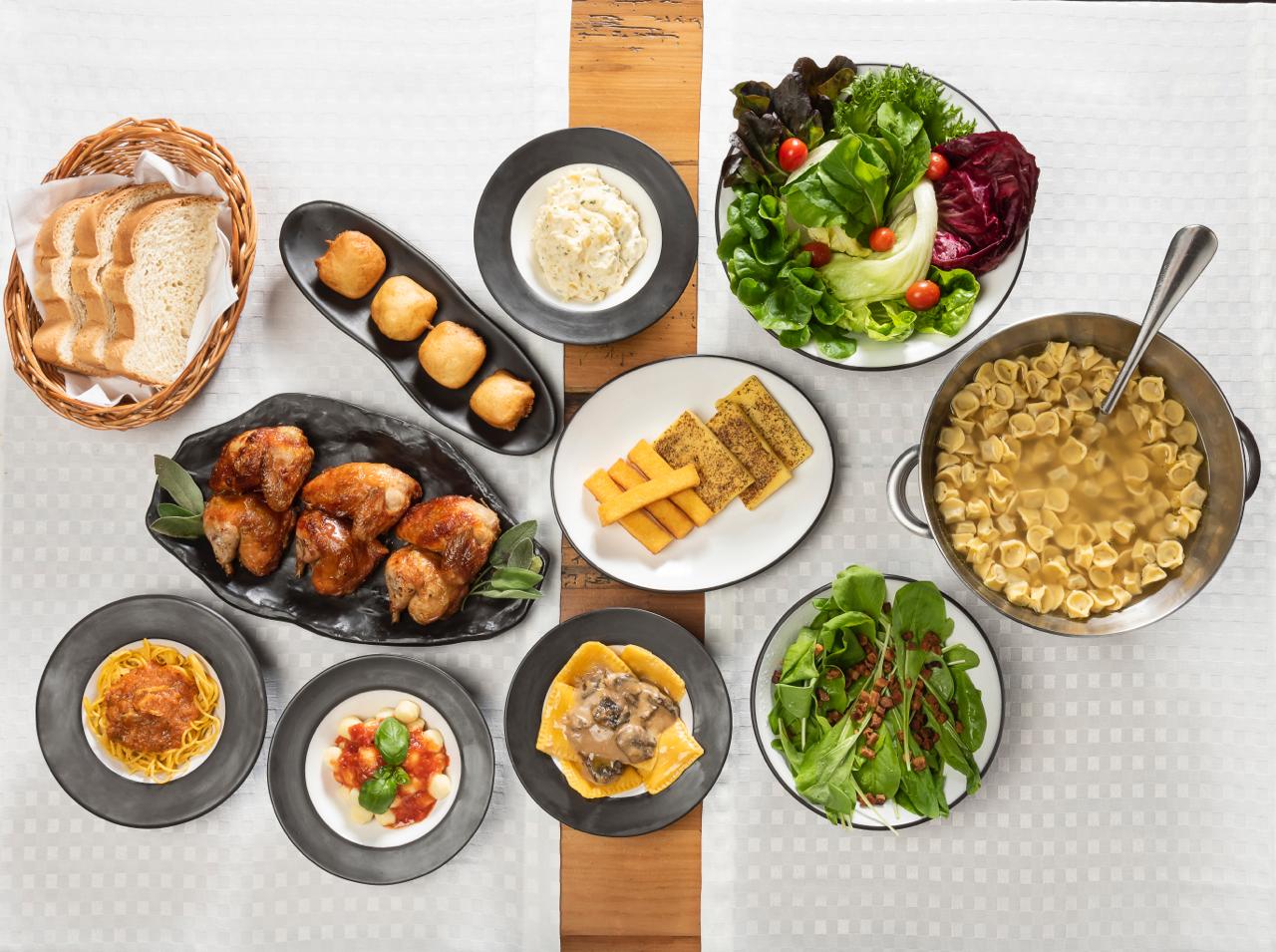 sequência do di paolo com pratos vistos de cima sobre a mesa: massas, bolinhos de queijo, saladas e galetos