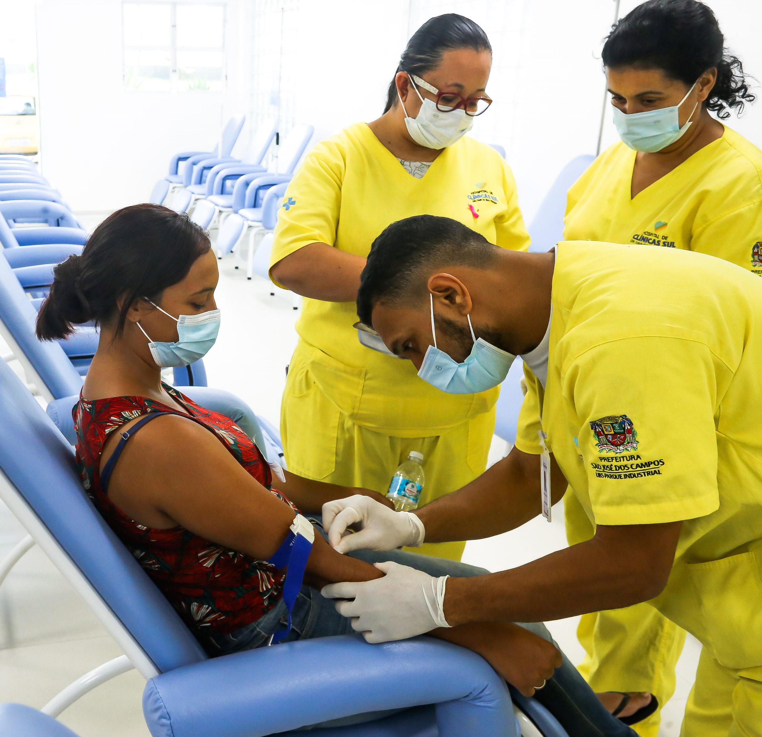 Mulher, sentada em cadeira, sendo atendida por enfermeiros em novo espaço de atendimento de dengue em São José