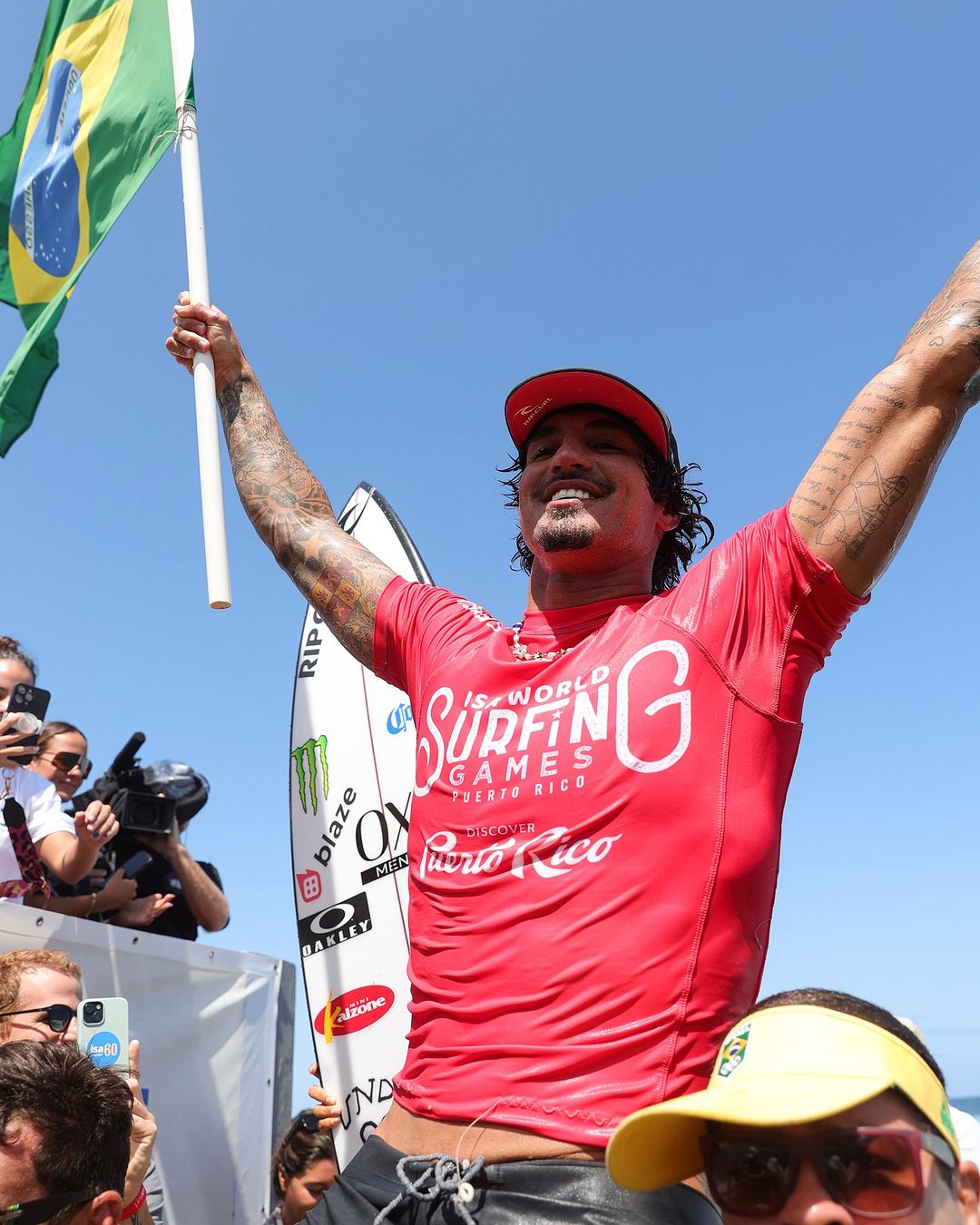 gabriel medina com braços abertos e sorrindo segurando a bandeira do brasil ao comemorar sua vitória no isa games em porto rico e consequentemente sua classificação para as olimpíadas de paris