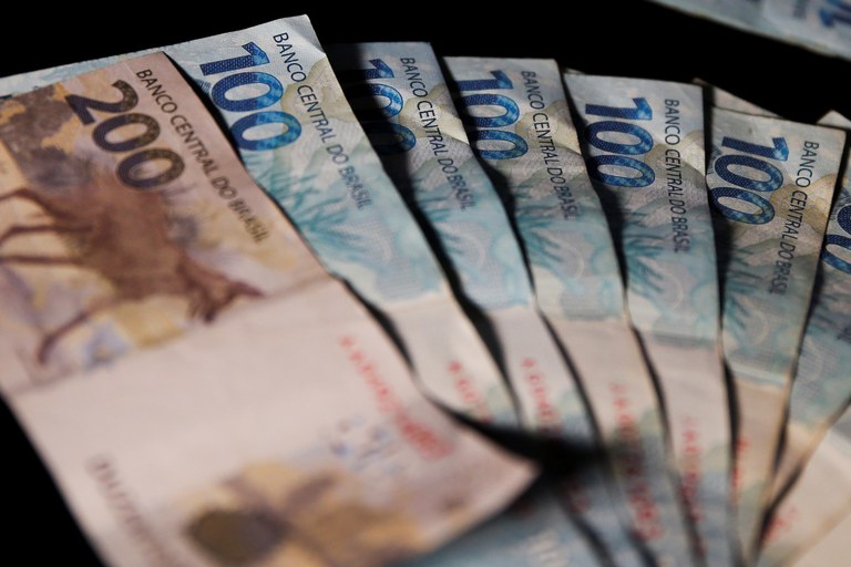 Notas de 200 e 100 reais, fazendo referência ao pagamento do 13° do INSS para segurados
