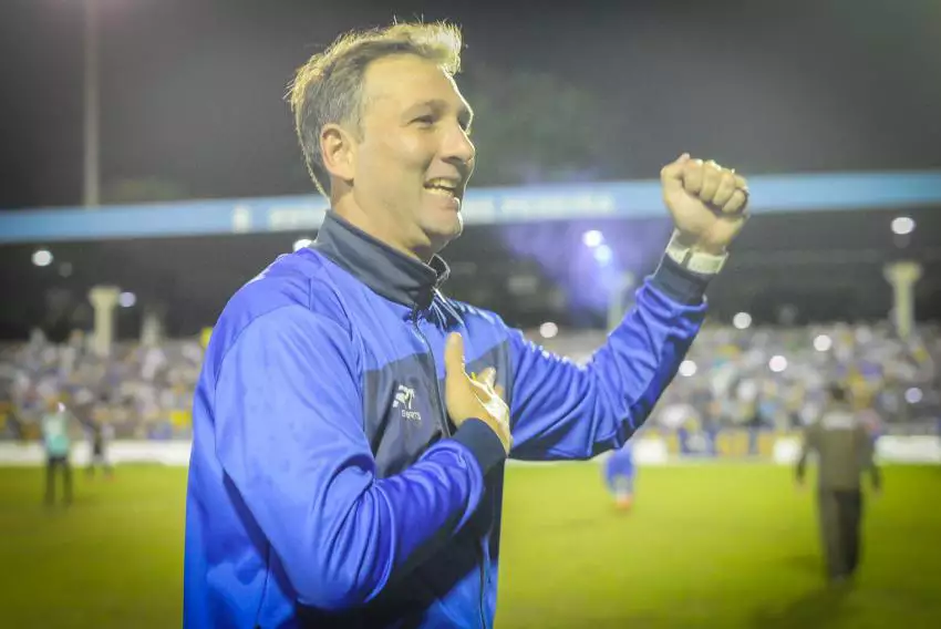 Ricardo Costa, técnico do São José, com mão no escudo do clube e sorrindo