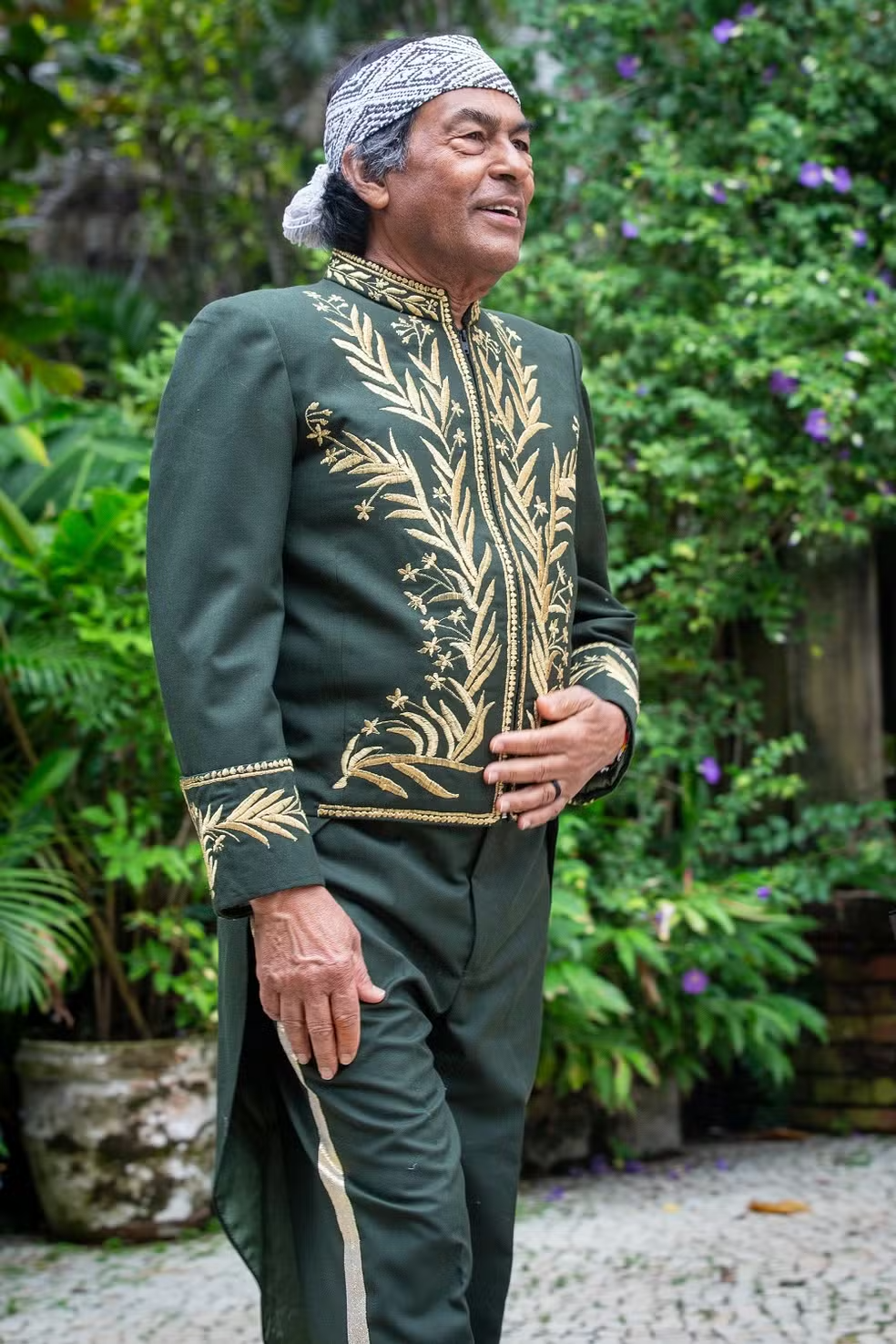 ailton krenak posando com fardão verde e dourado da ABL em jardim, com fundo repleto de moitas bem verdes atrás