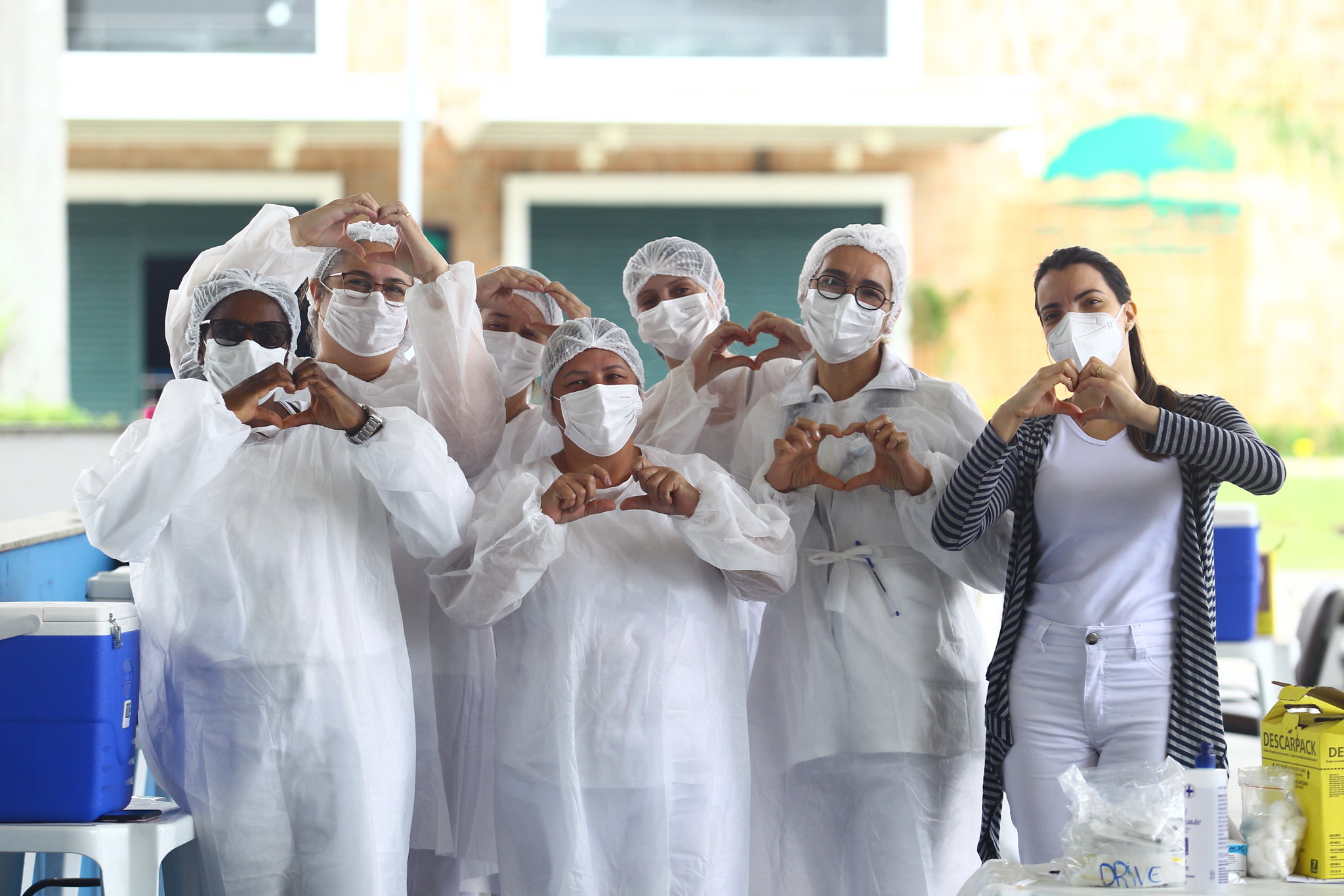 profissionais da saúde na pandemia de jaleco, touca e máscara brancos posando para foto fazendo coração com as mãos
