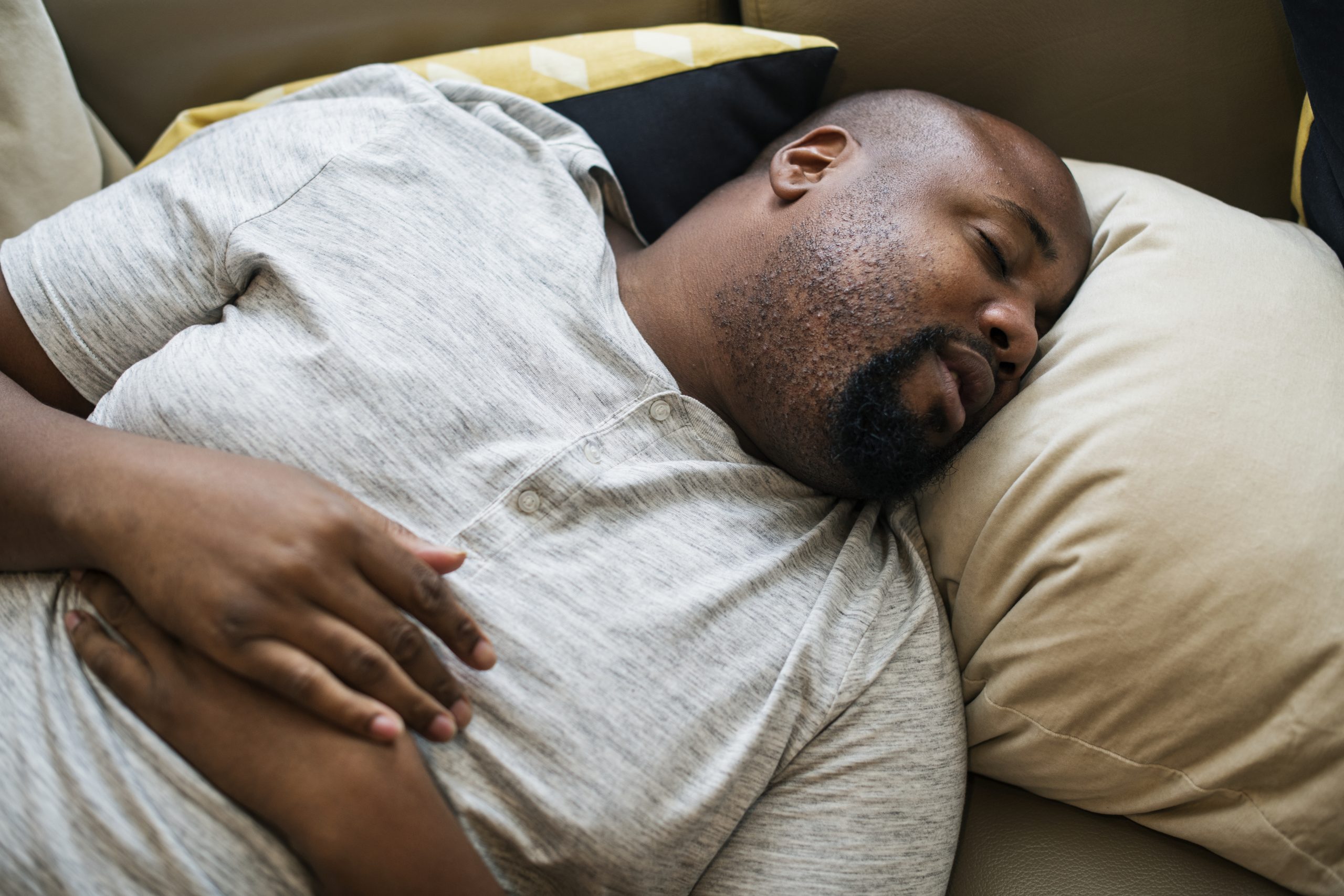 homem negro dormindo de barriga para cim, com as mãos sobre o peito, e com cabeça virada para a direita